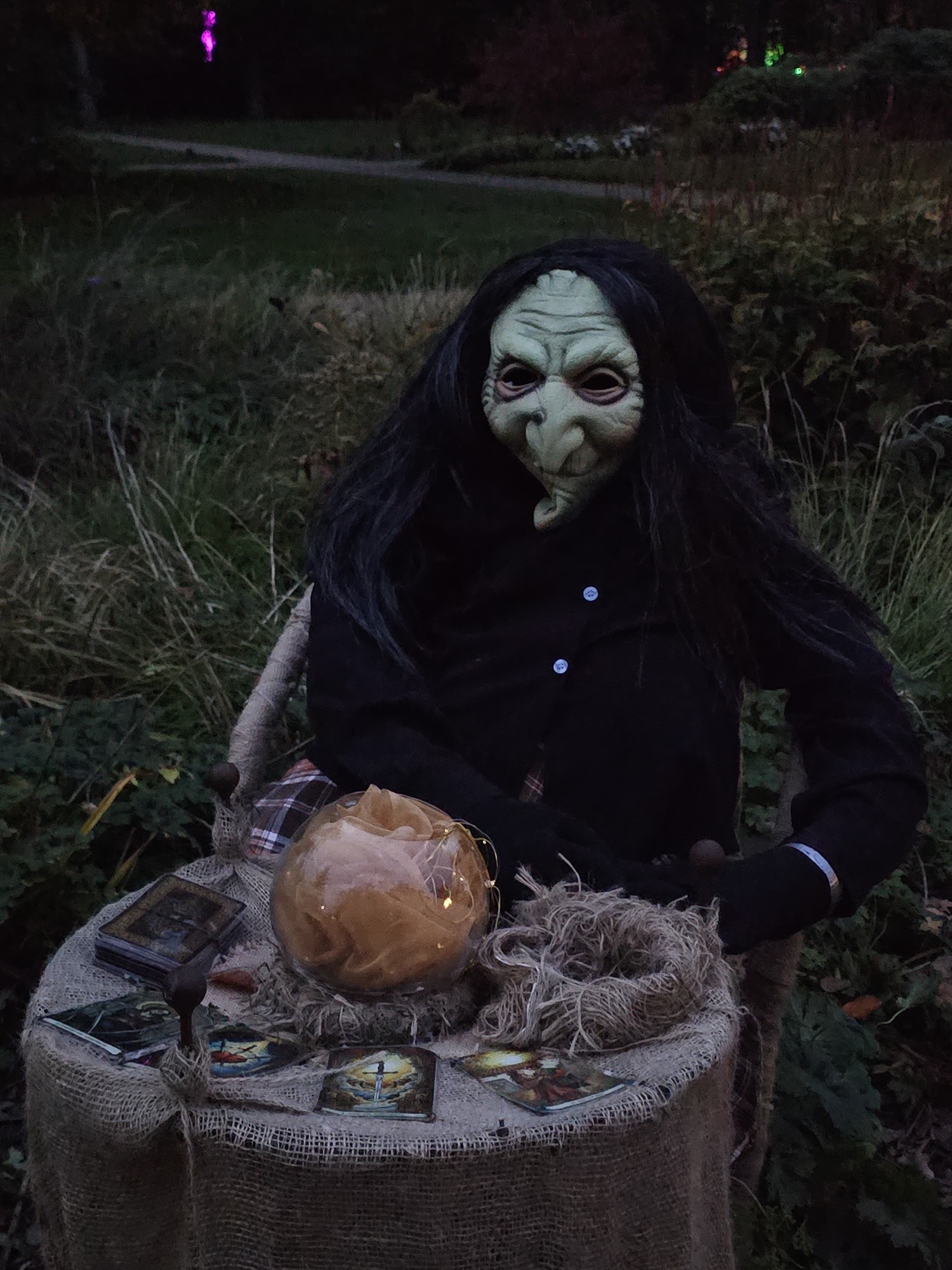 Hexe mit Maske an einem Tisch mit Tarotkarten und Kürbis
